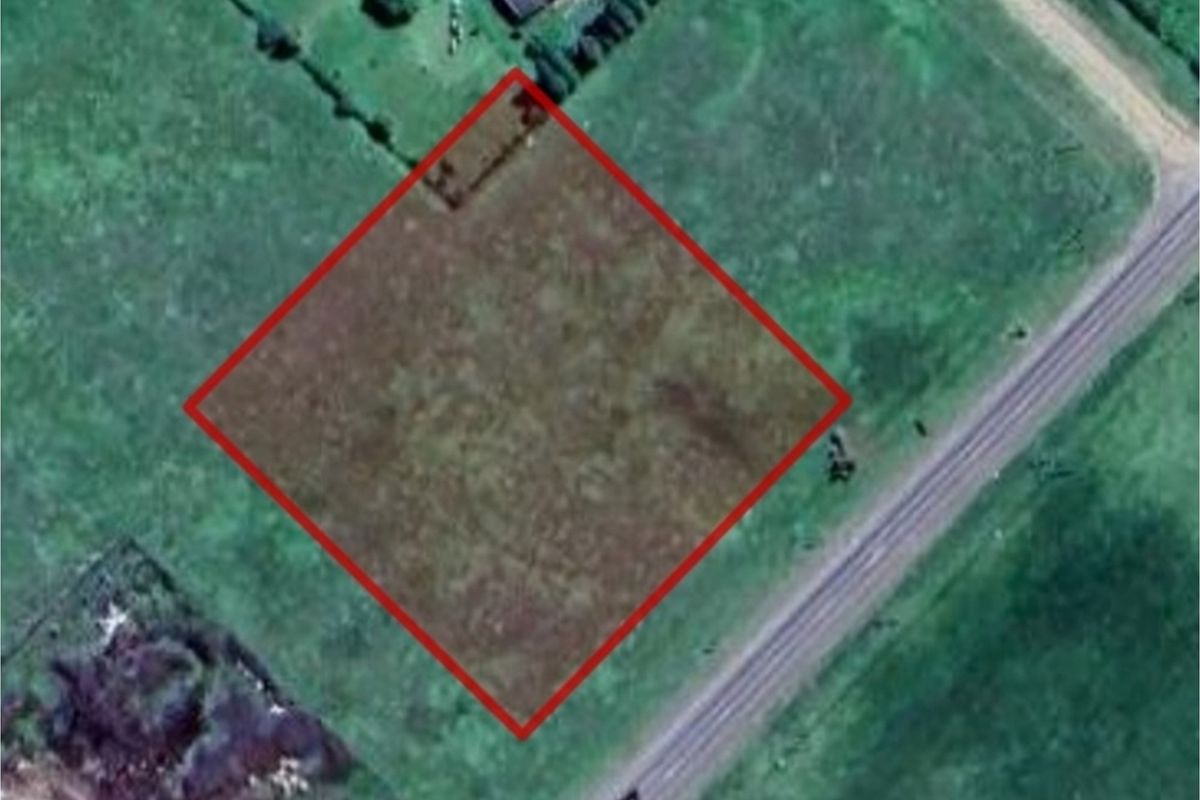 Aerial view of a vacant residential plot of land, clearly outlined in red, situated adjacent to a road.