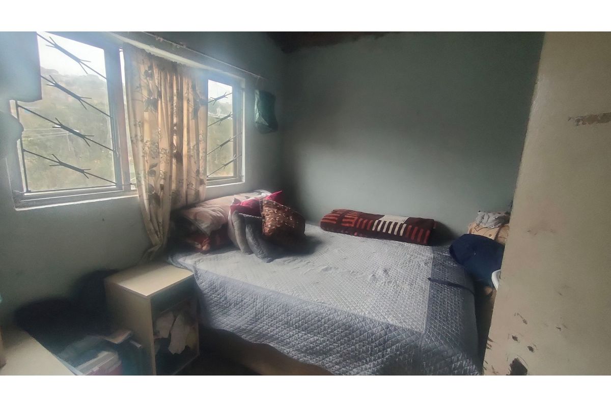 A compact bedroom featuring a window with security bars and basic wall finishes, offering a functional space for rest.