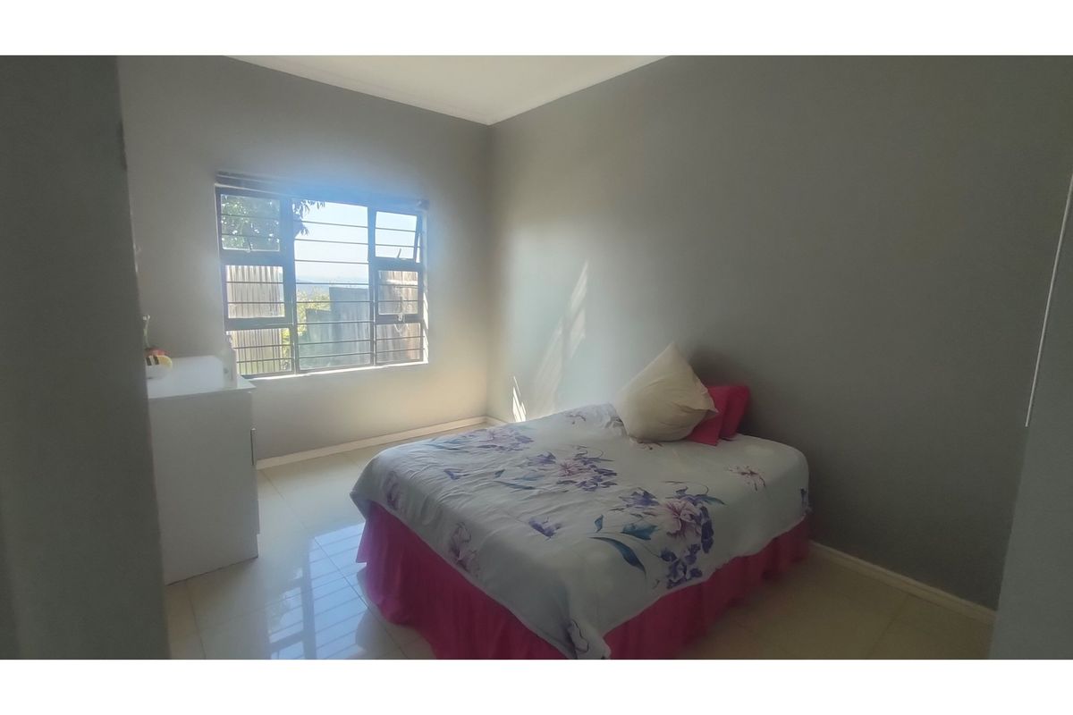A simple bedroom featuring tiled flooring and a window with security bars, offering a functional and neutral living space.