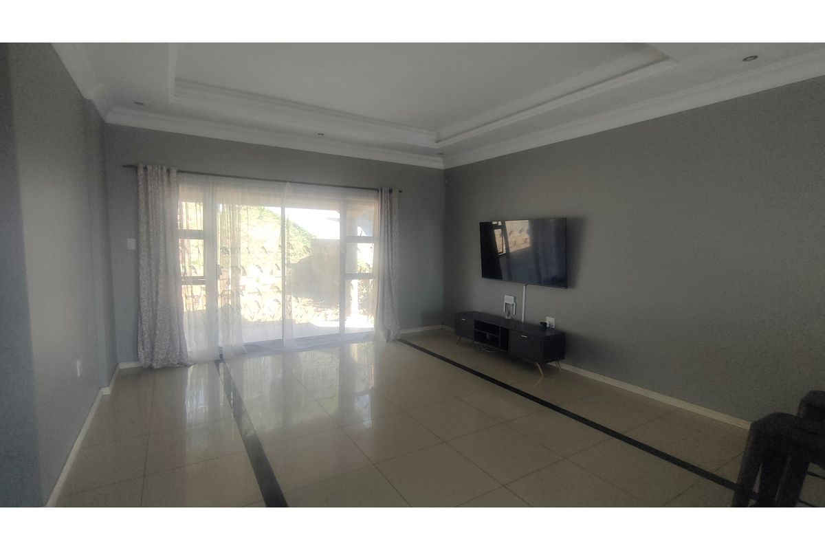 Spacious living room featuring large sliding glass doors, neutral grey walls, tiled flooring with decorative inlay, and a modern recessed ceiling design.