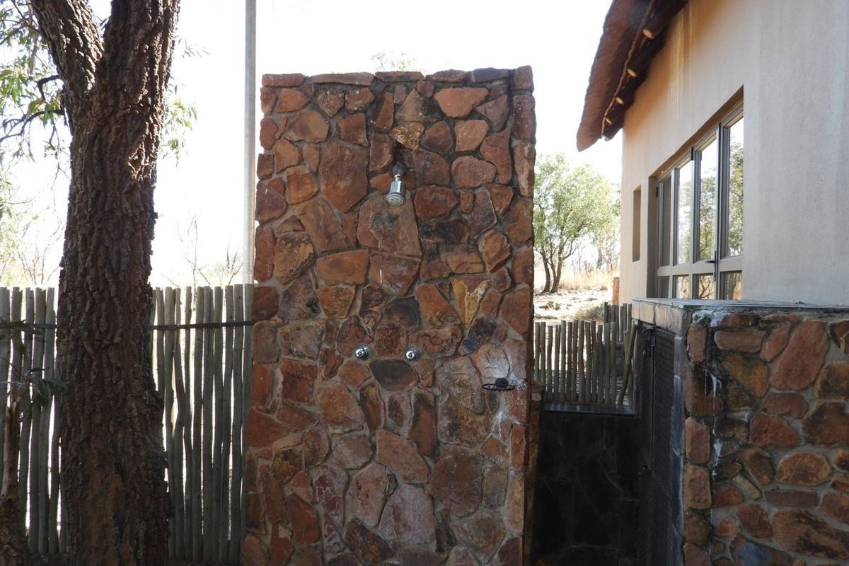 Outdoor shower area featuring a rustic stone-clad wall with integrated plumbing fixtures, situated adjacent to the main dwelling.