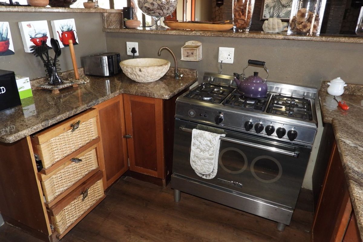 A kitchen area featuring a stainless steel gas stove, granite countertops, and a stone vessel sink with rustic cabinetry.