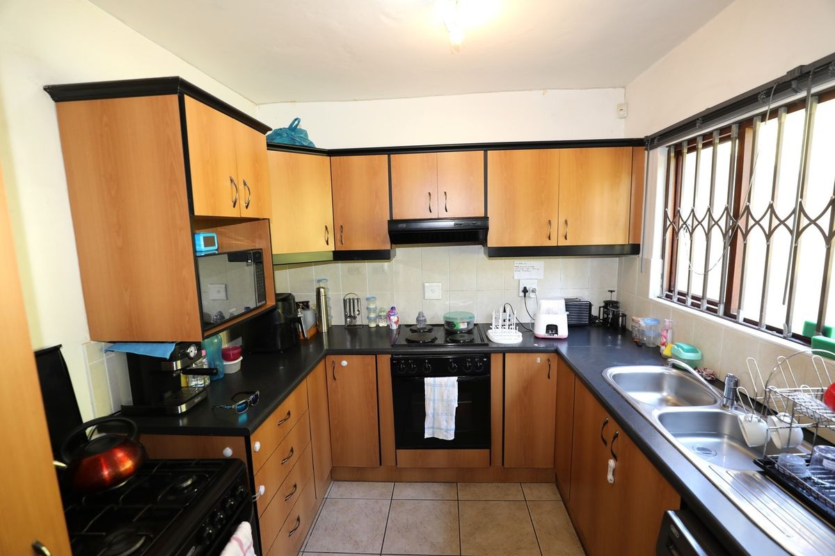 A functional U-shaped kitchen featuring wood-look cabinetry, dark laminate countertops, a built-in oven, extractor fan, and a double stainless steel sink.