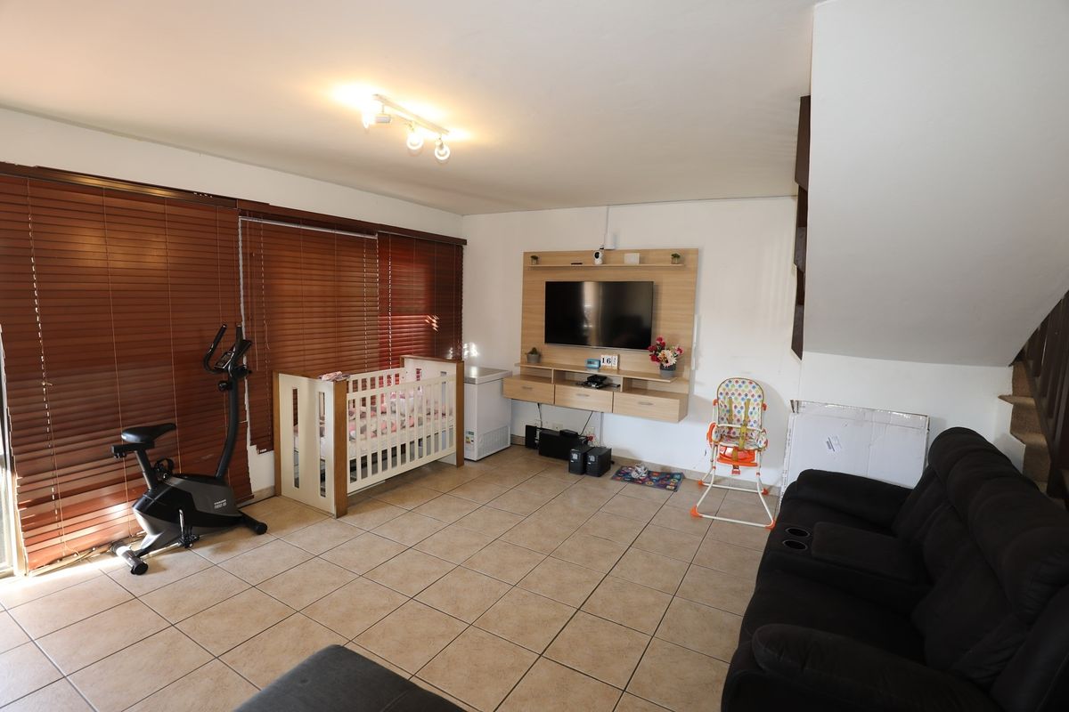 A spacious living area featuring tiled flooring, wooden venetian blinds, and a built-in media console unit.