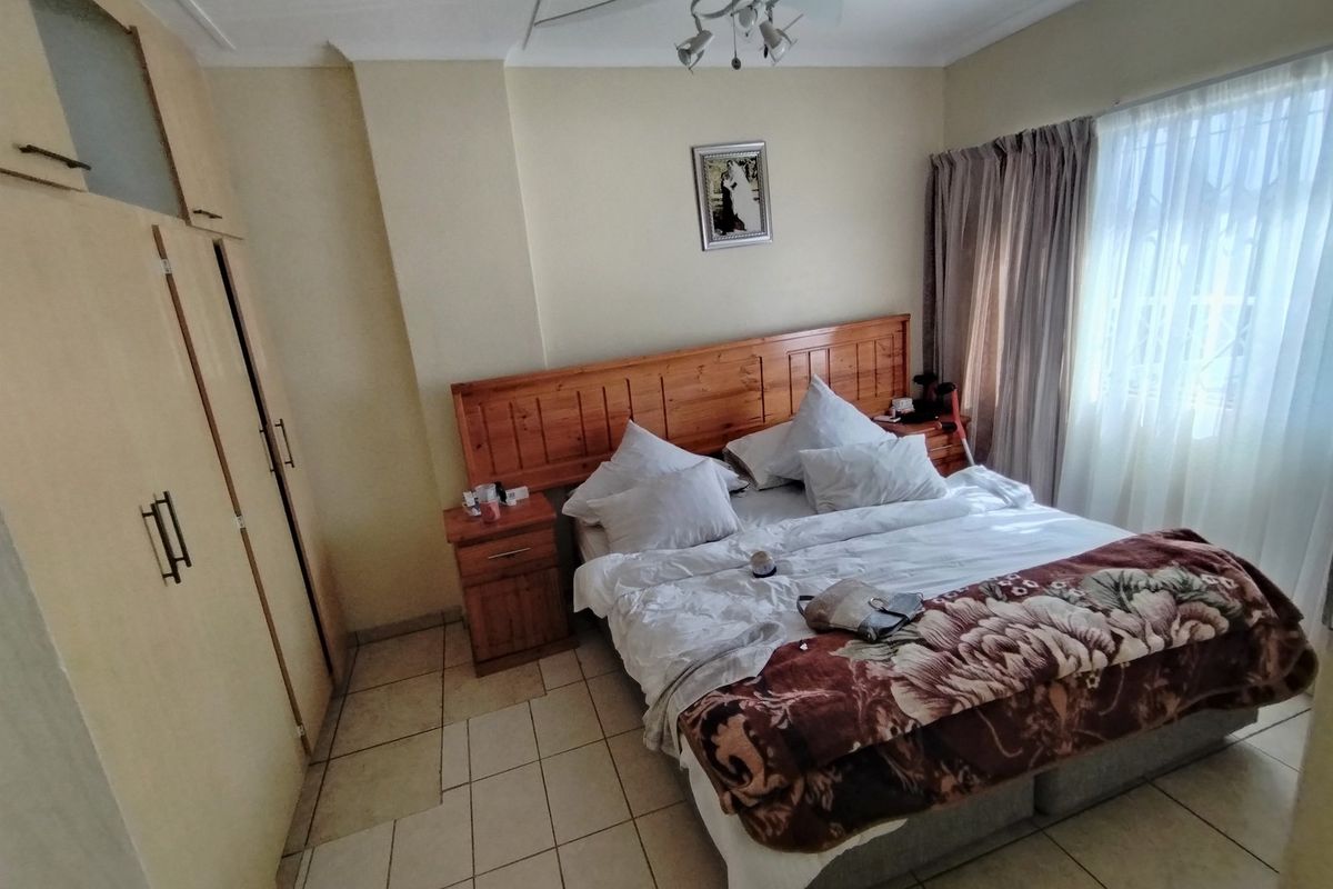 A bedroom featuring built-in wooden cupboards, tiled flooring, and a wooden headboard with matching bedside pedestals.