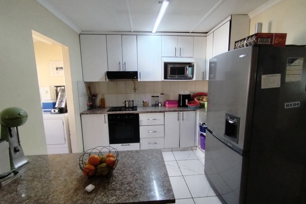Functional kitchen featuring white cabinetry, built-in oven, hob, extractor fan, and granite-look countertops, with an adjacent scullery area visible.