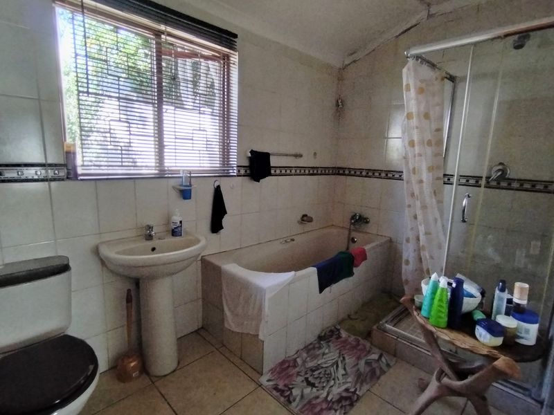 A dated bathroom featuring a pedestal basin, built-in bathtub, and separate shower enclosure, requiring renovation to update finishes and address visible wear.