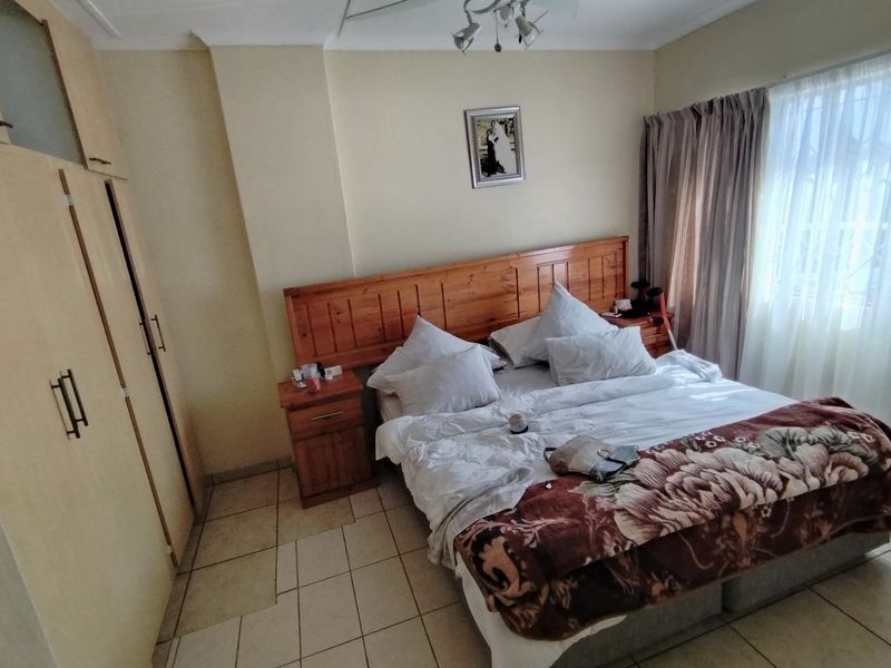 A functional bedroom featuring built-in wooden cupboards, tiled flooring, and a window with curtain tracks.