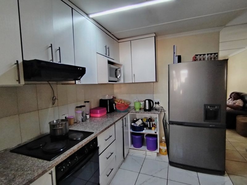 Functional kitchen featuring white cabinetry, laminate countertops, built-in oven, electric hob, and tiled flooring, offering a practical layout for daily meal preparation.