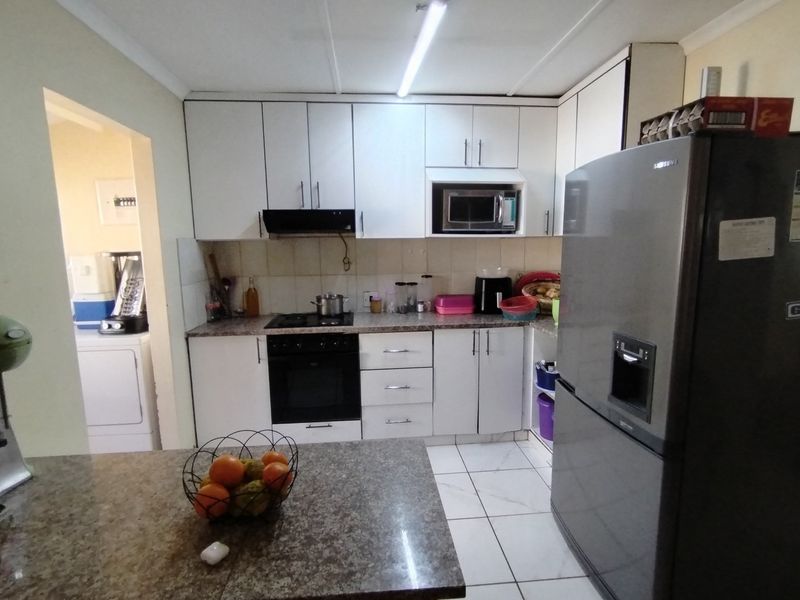 A functional kitchen featuring white cabinetry, laminate countertops, built-in oven, hob, and extractor fan, with tiled flooring and an adjacent laundry area.