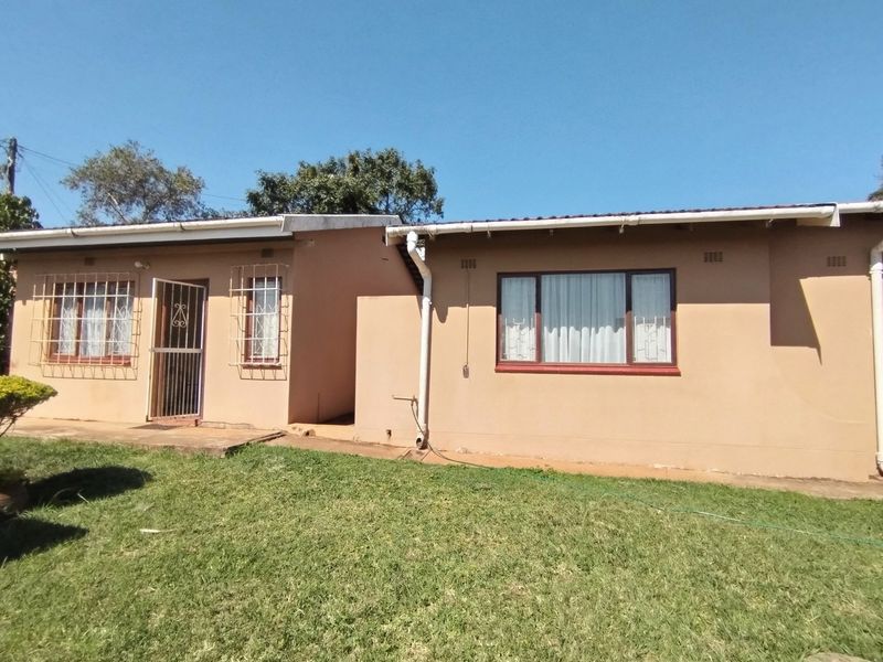 Rear exterior view of the house featuring a lawn, concrete apron, and security bars on windows and doors.