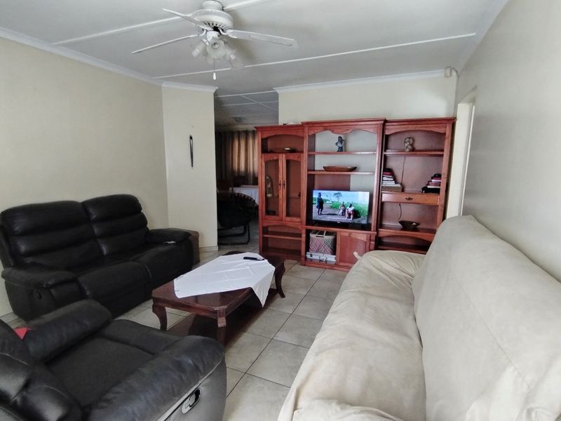 A living room featuring tiled flooring, a ceiling fan, and a built-in wooden shelving unit, offering a functional and comfortable living space.