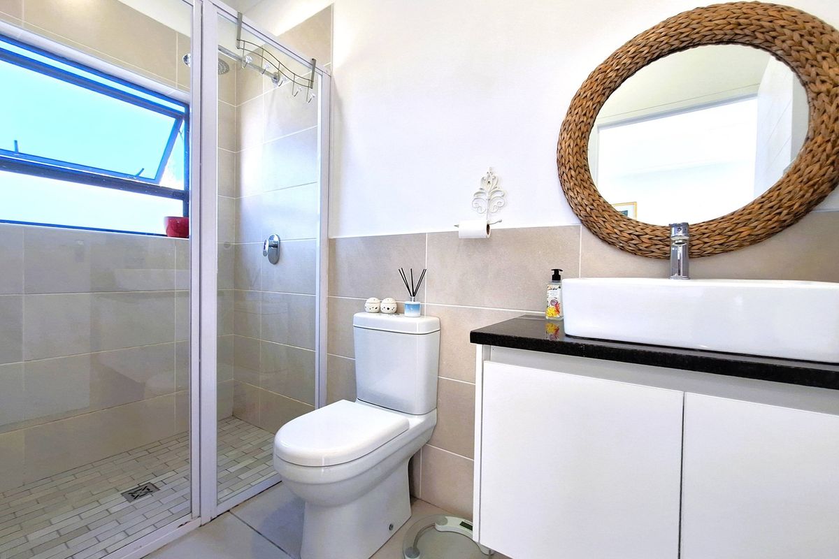 A modern bathroom featuring a glass-enclosed shower, a white vanity with a black countertop, a vessel sink, and neutral wall tiling.