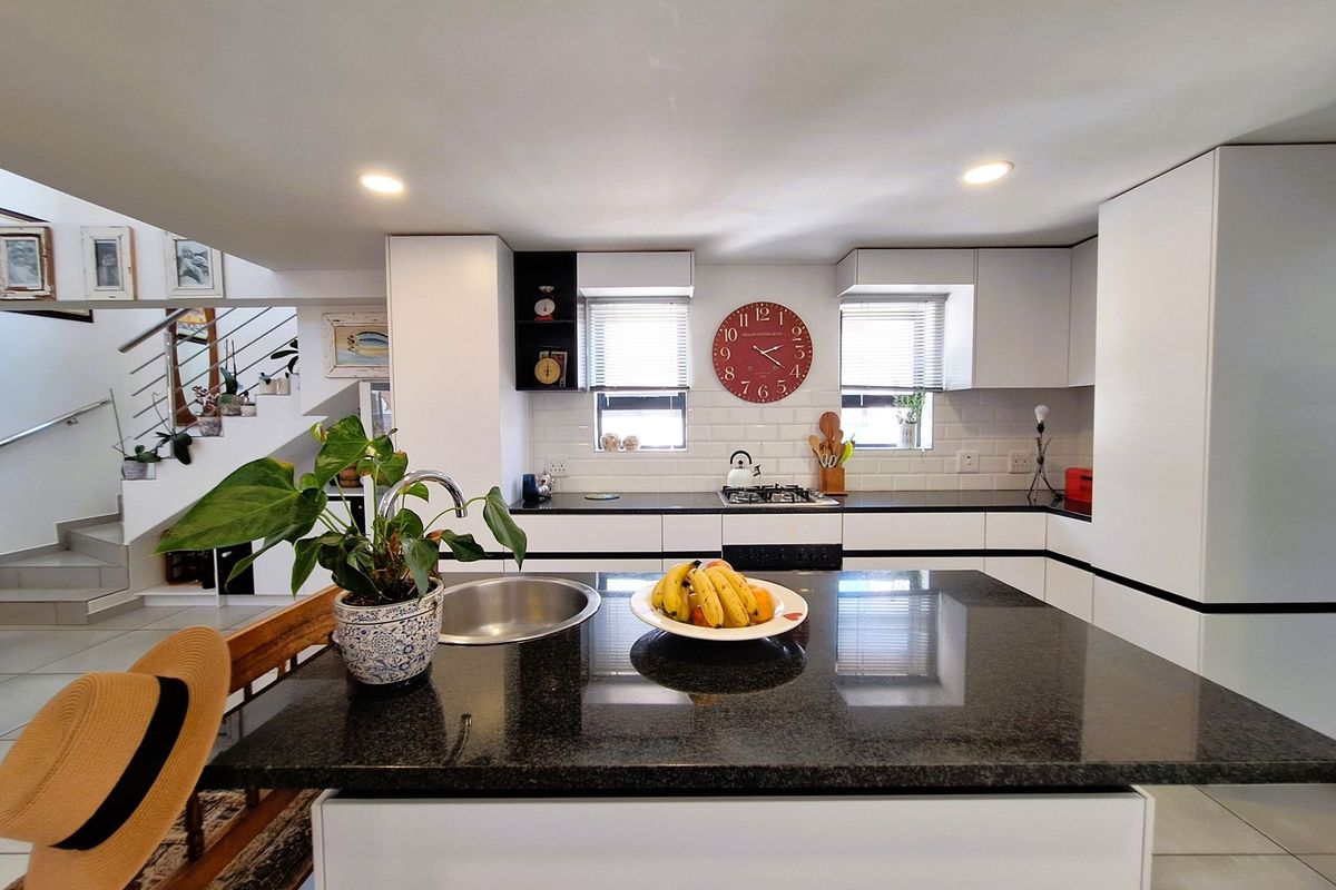 Modern kitchen featuring a central island with a granite countertop, sleek white cabinetry, subway tile backsplash, and integrated gas hob.