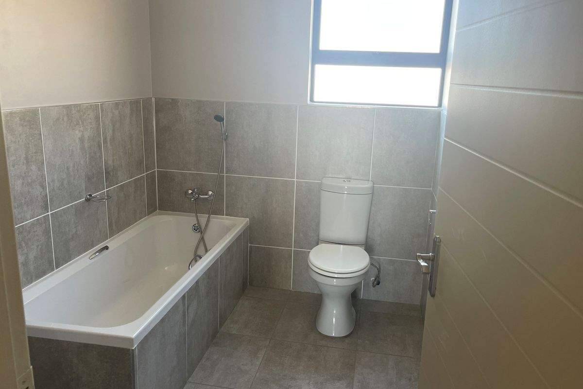 A modern bathroom featuring grey floor-to-ceiling wall tiles, a built-in bathtub with a handheld shower mixer, and a standard white toilet.
