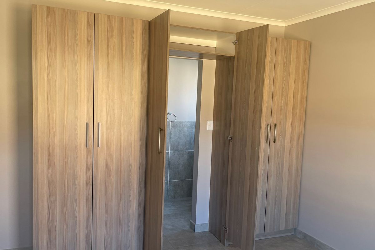 A bedroom featuring built-in wooden cupboards with a central walk-through passage leading to an adjoining bathroom.