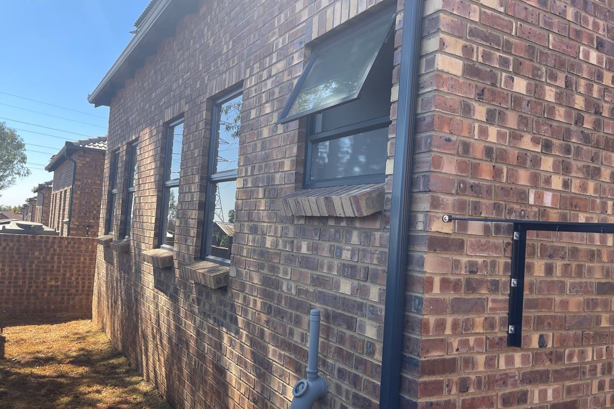 Side exterior view of the townhouse featuring face brick facade, dark-framed windows, and integrated guttering system.