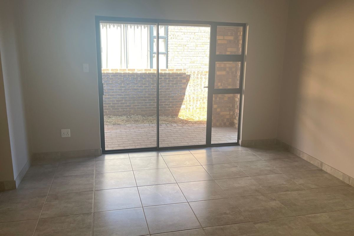 An empty living room featuring neutral floor tiles and a large sliding glass door providing direct access to a paved outdoor area.