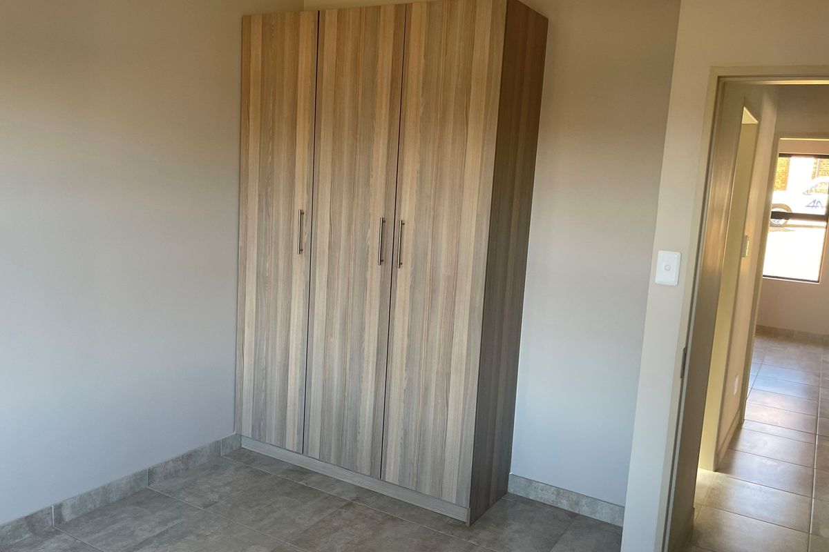 A bedroom featuring built-in wooden cabinetry and tiled flooring, with a view into an adjacent hallway.