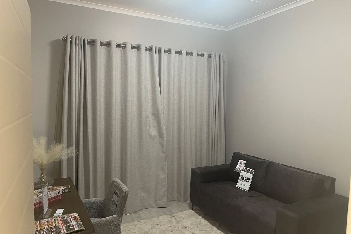 A neutral-toned living room featuring large window curtains and tiled flooring, providing a clean and versatile space.