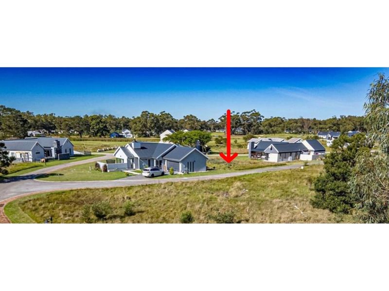 An aerial view of a vacant residential plot situated within a developed estate, featuring road access and surrounding established homes.