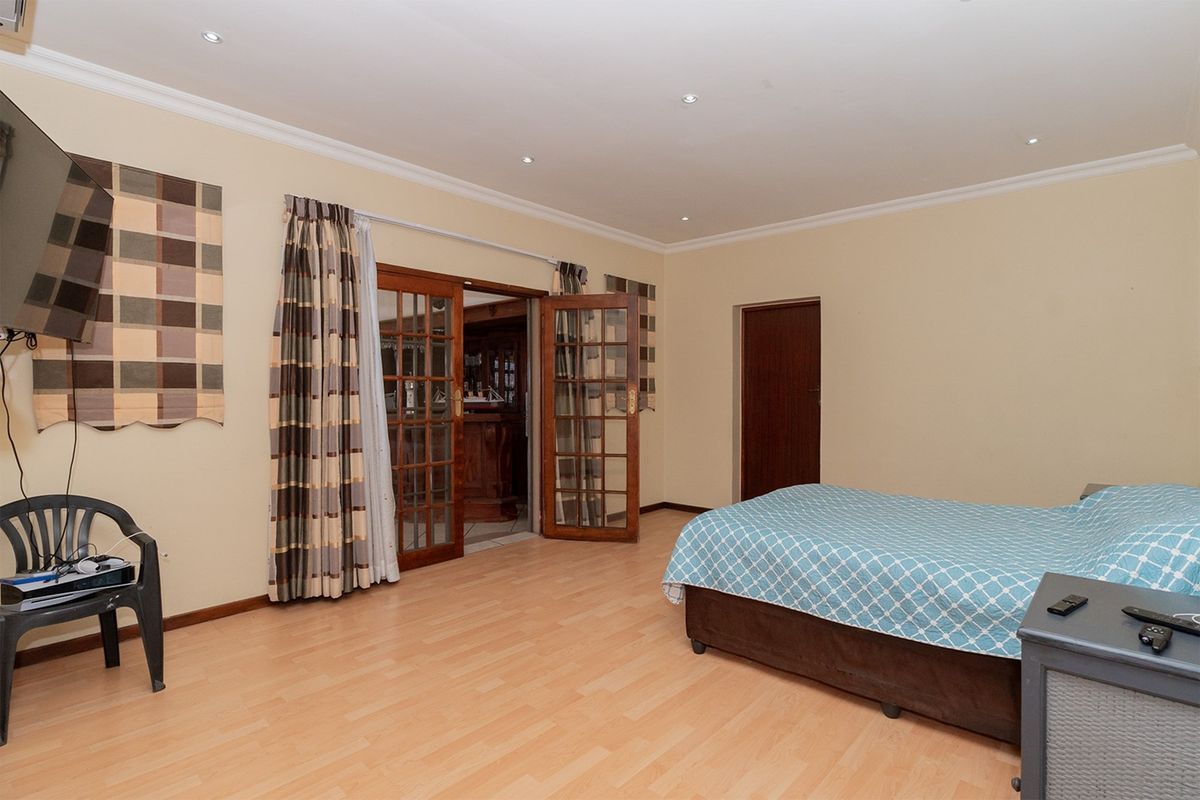 Spacious bedroom featuring laminate flooring, recessed ceiling lighting, and double wooden doors leading to an adjacent room.