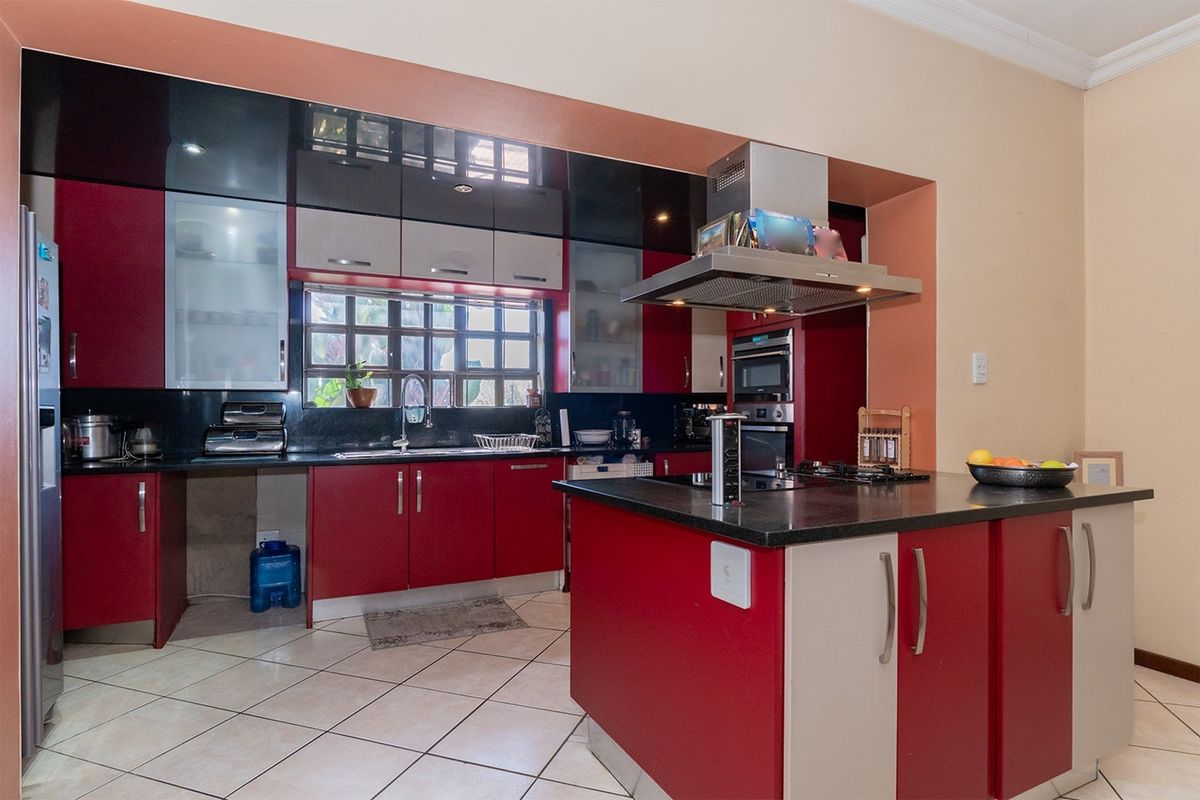 A functional kitchen featuring a central island, built-in oven, extractor fan, and ample cabinetry with a contrasting red and black design.