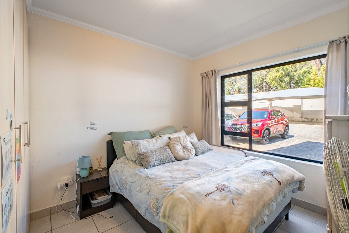 A bedroom featuring tiled flooring, built-in cupboards, and a large window providing natural light and views of the parking area.