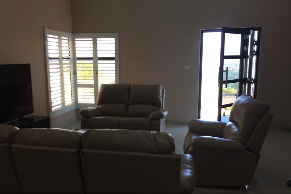 A living room featuring tiled flooring, plantation shutters, and direct access to an outdoor area through a glass door.
