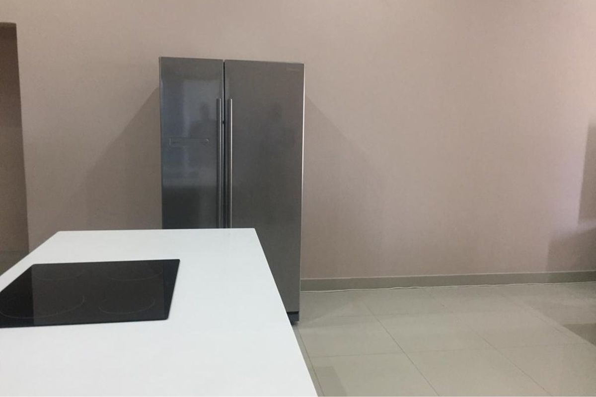 A minimalist kitchen area featuring a central island with a built-in electric cooktop and neutral tiled flooring.