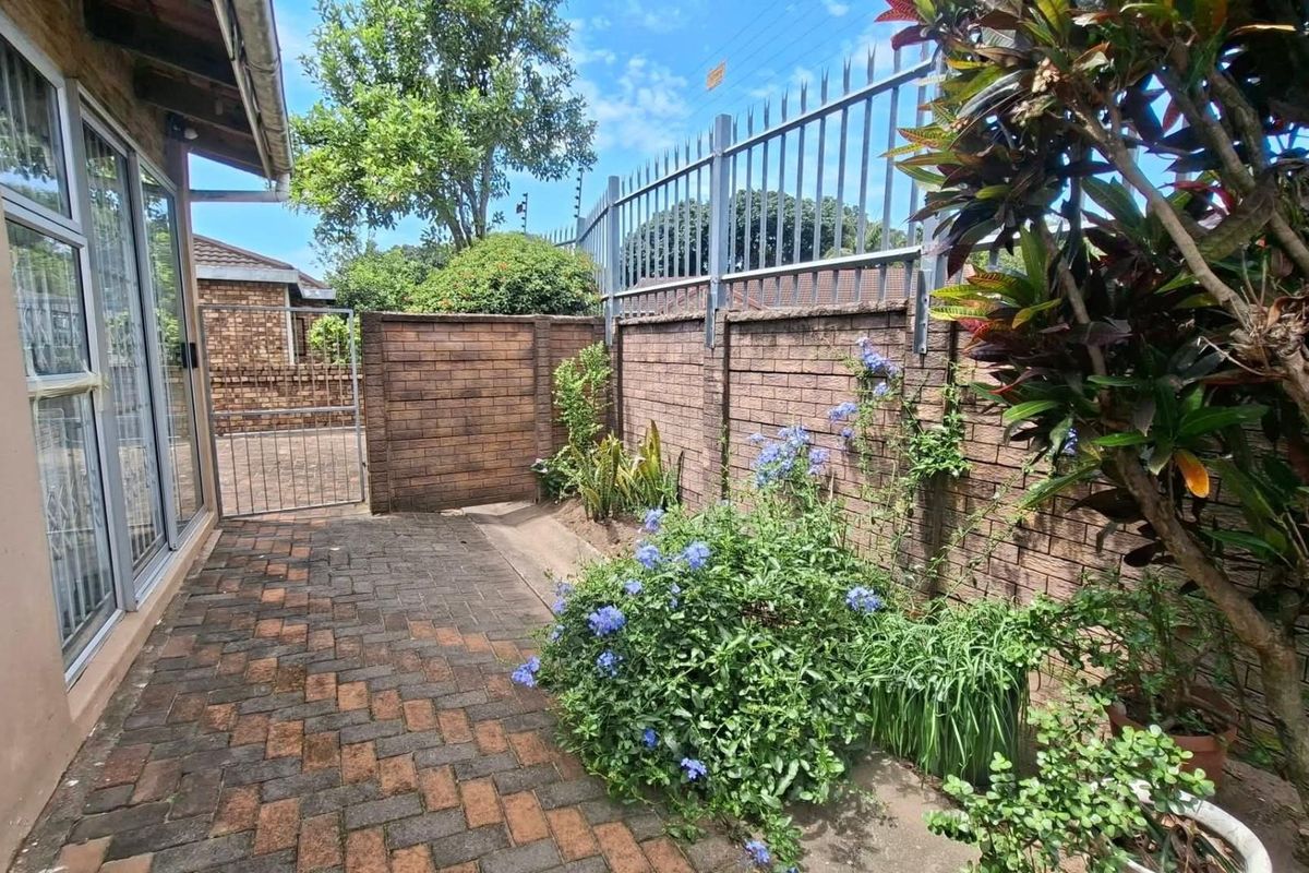 A private rear courtyard featuring paved flooring, brick boundary walls, and secure metal perimeter fencing with established garden greenery.