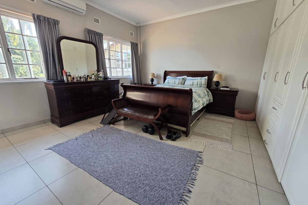 Spacious bedroom featuring neutral tiled flooring, built-in cupboards, and a wall-mounted air conditioning unit, offering a comfortable and functional living space.