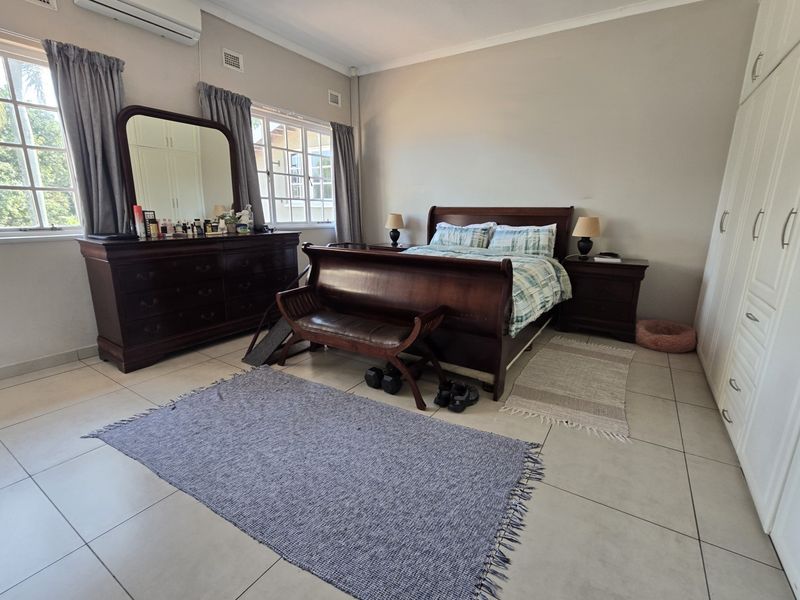 Spacious bedroom featuring neutral tiled flooring, built-in cupboards, and a wall-mounted air conditioning unit, offering a comfortable and functional living space.