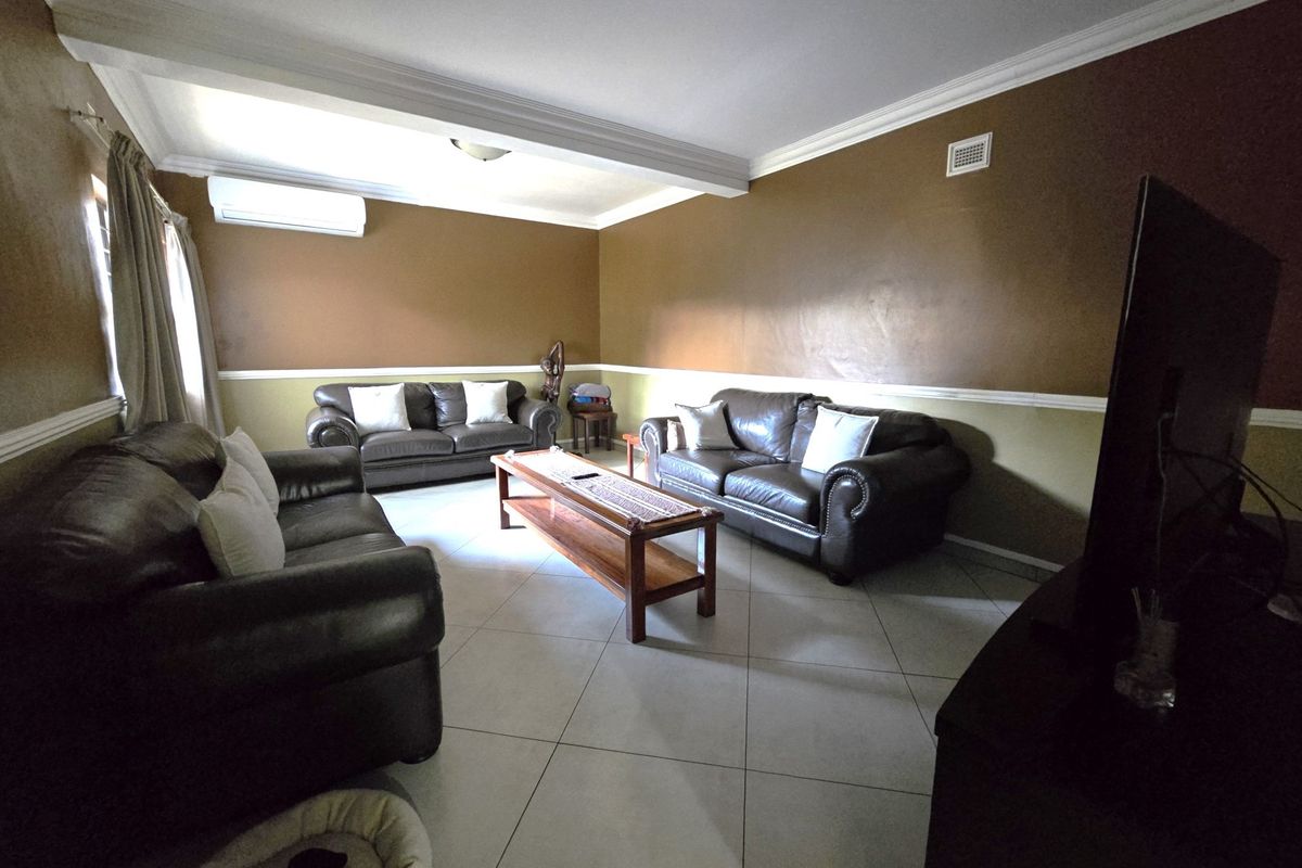 A spacious living room featuring tiled flooring, crown molding, and a wall-mounted split-system air conditioner.