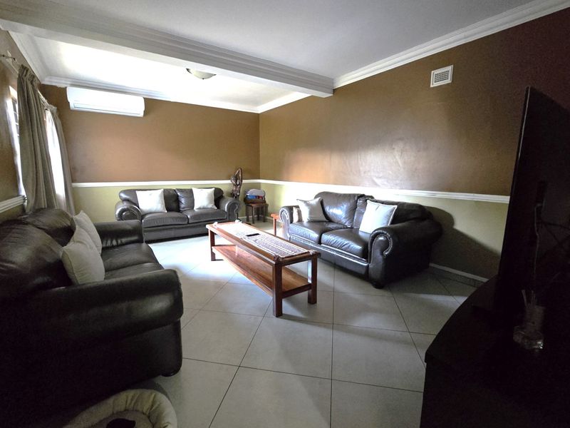 A spacious living room featuring tiled flooring, crown molding, and a wall-mounted split-system air conditioner.