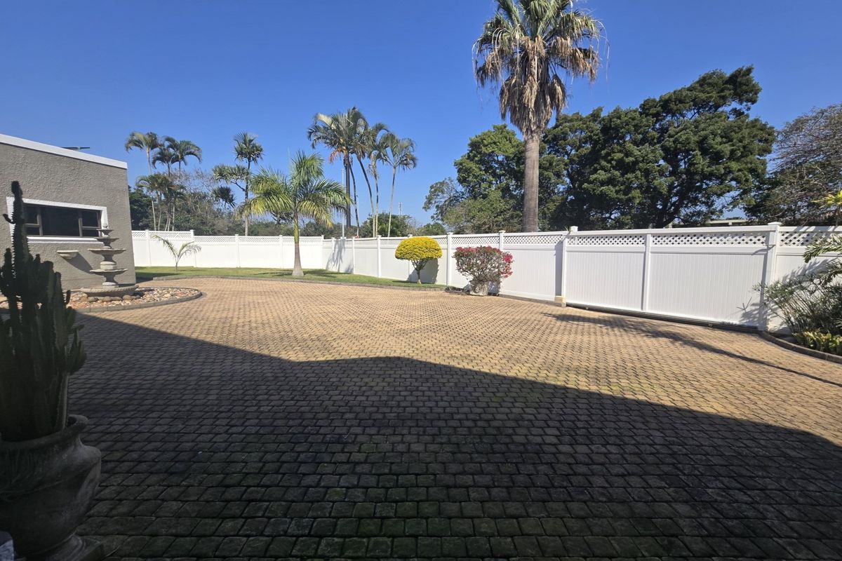 A spacious rear courtyard featuring extensive paved areas, a decorative stone water feature, and secure white vinyl privacy fencing surrounded by mature trees.