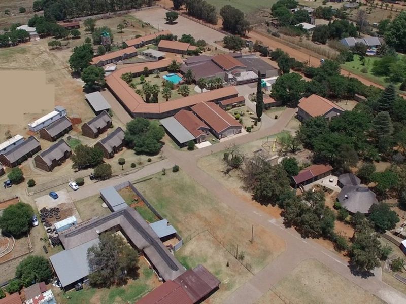 Aerial view of a lodge property featuring multiple buildings, a central swimming pool, paved pathways, and extensive landscaped grounds.