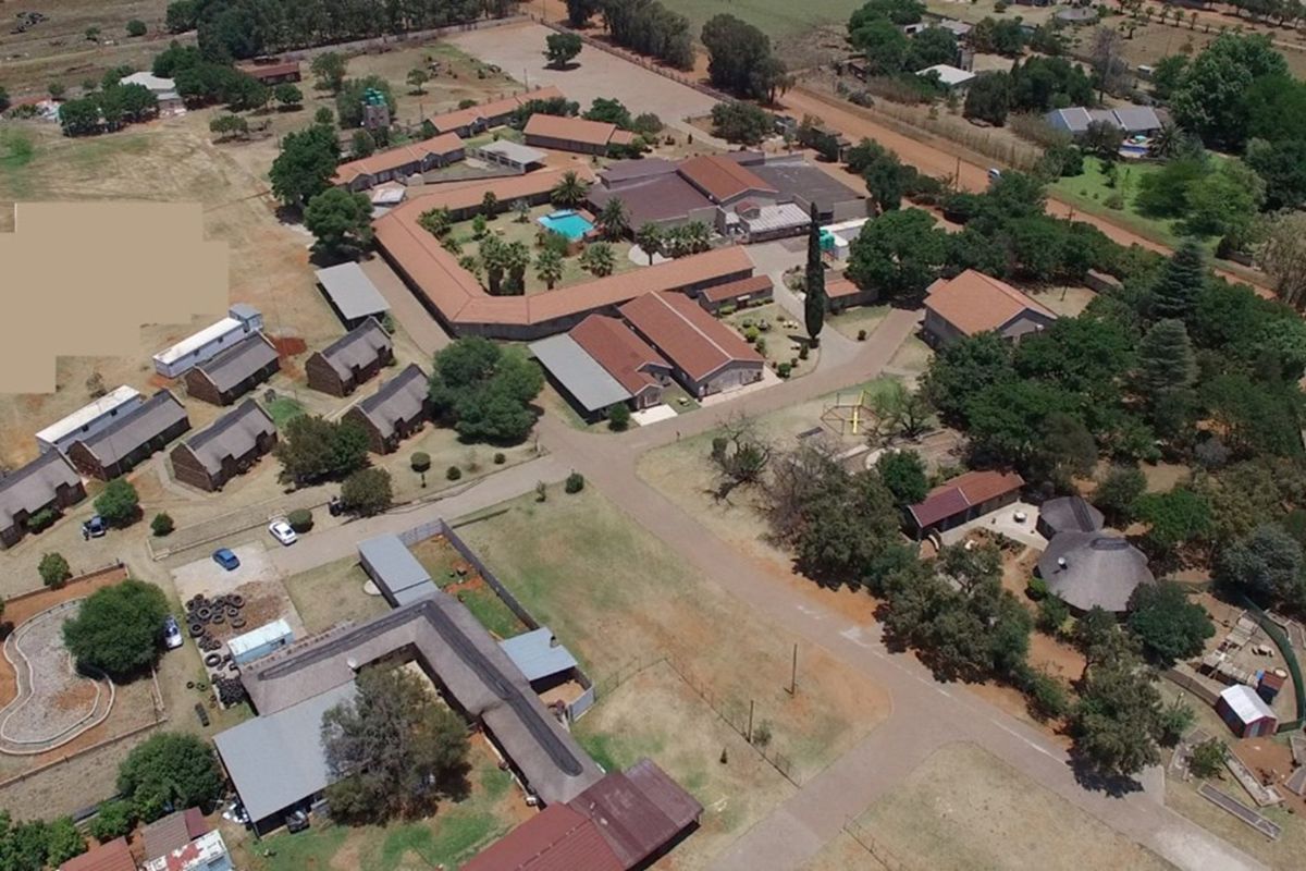 Aerial view of a lodge property featuring multiple buildings, a central swimming pool, paved pathways, and extensive landscaped grounds.