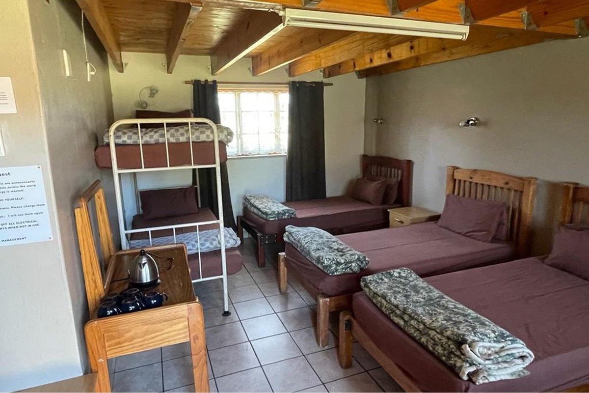 A multi-bed lodge bedroom featuring exposed timber ceiling beams, tiled flooring, and a standard casement window.