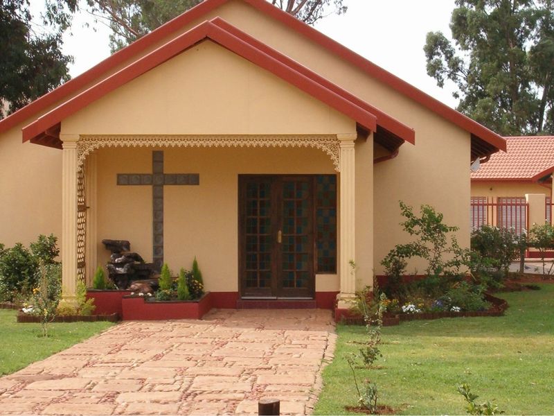 Front view of a lodge building featuring a covered porch, decorative ironwork, stone walkway, and a well-maintained garden setting.