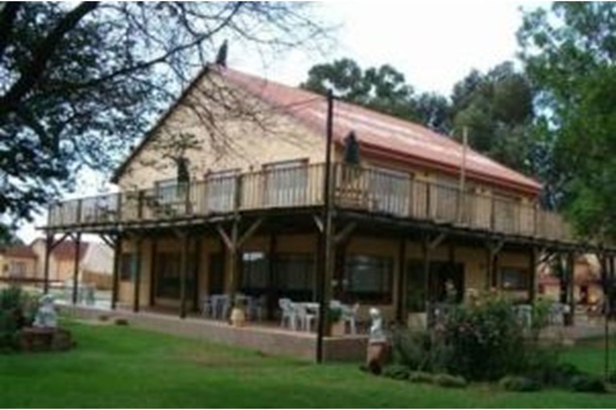 A lodge-style building featuring a wrap-around timber deck and balcony, set within a landscaped garden area.
