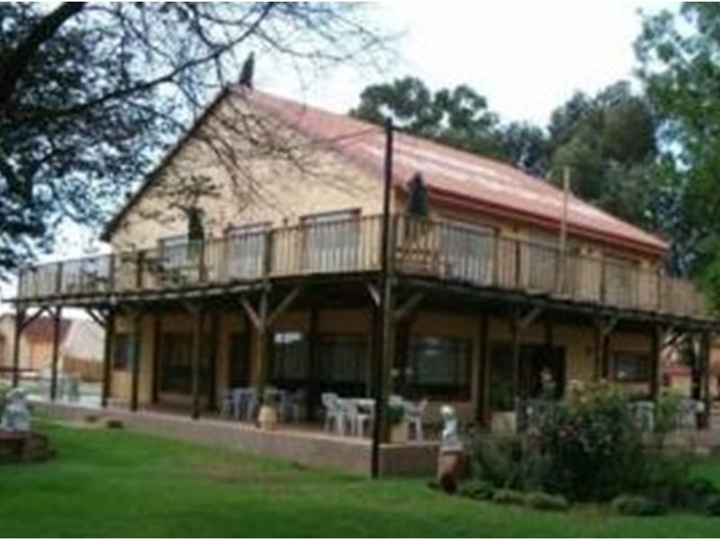 A lodge-style building featuring a wrap-around timber deck and balcony, set within a landscaped garden area.