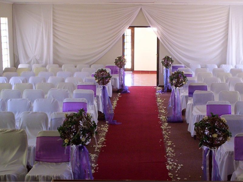 A large event space set up for a ceremony, featuring a central aisle, neutral walls, and a glass block window.