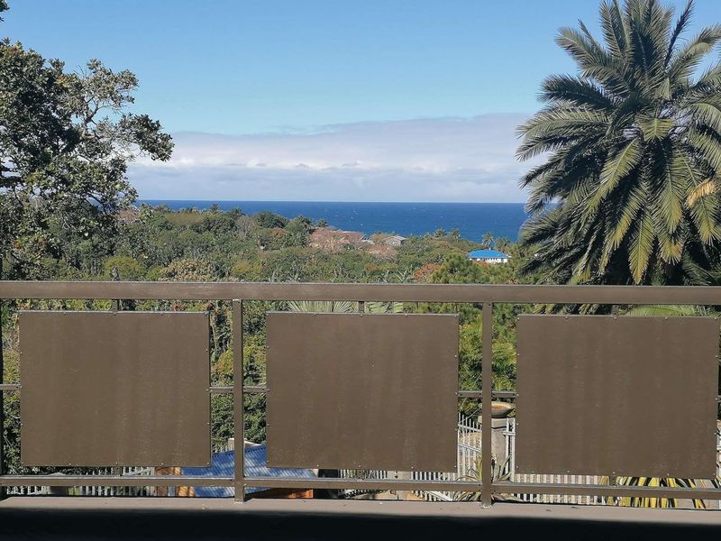 A scenic elevated view of the ocean and surrounding coastal landscape, framed by a modern metal balustrade with privacy panels.