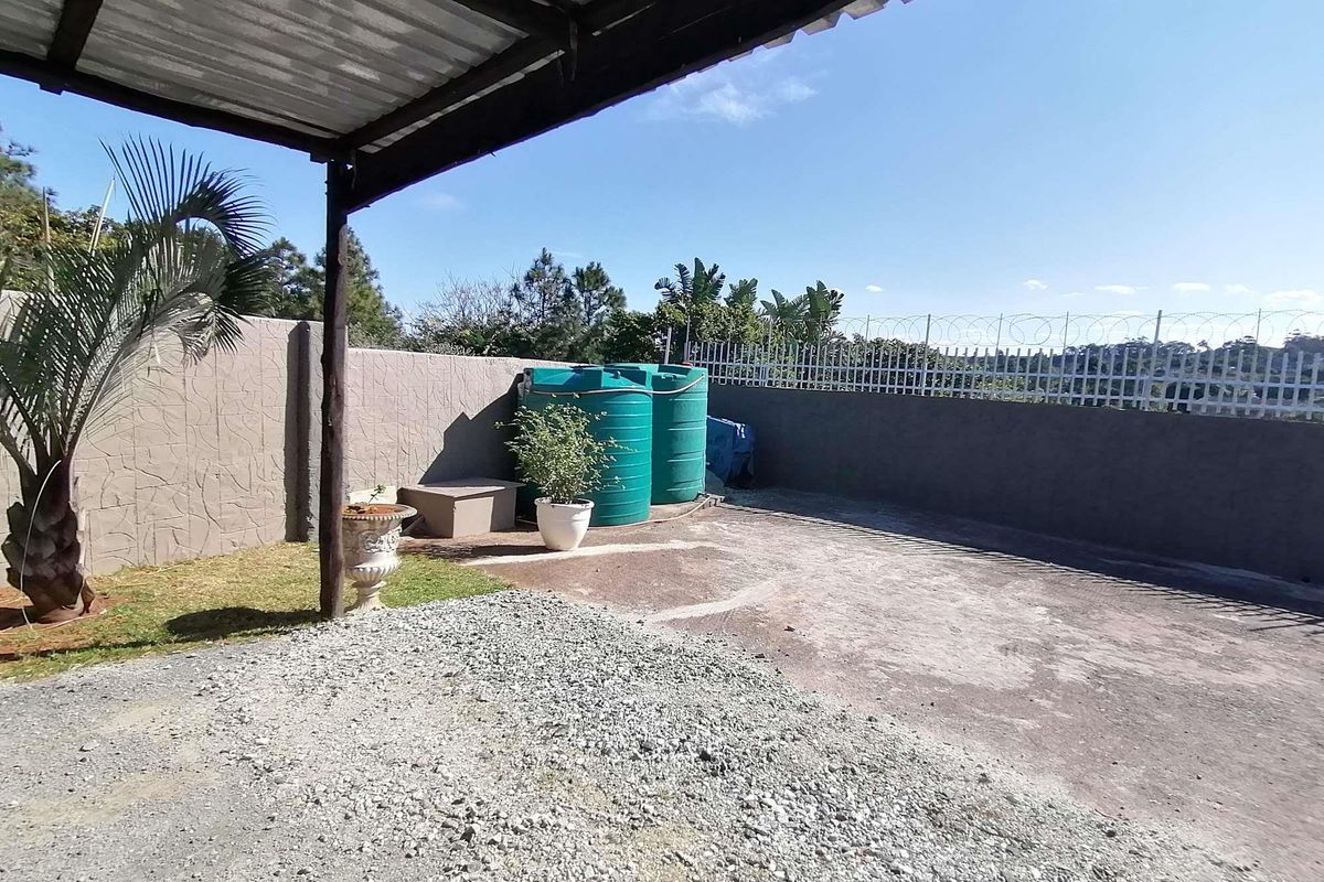 Rear outdoor area featuring a covered patio, concrete paving, perimeter wall with security fencing, and installed water storage tanks.