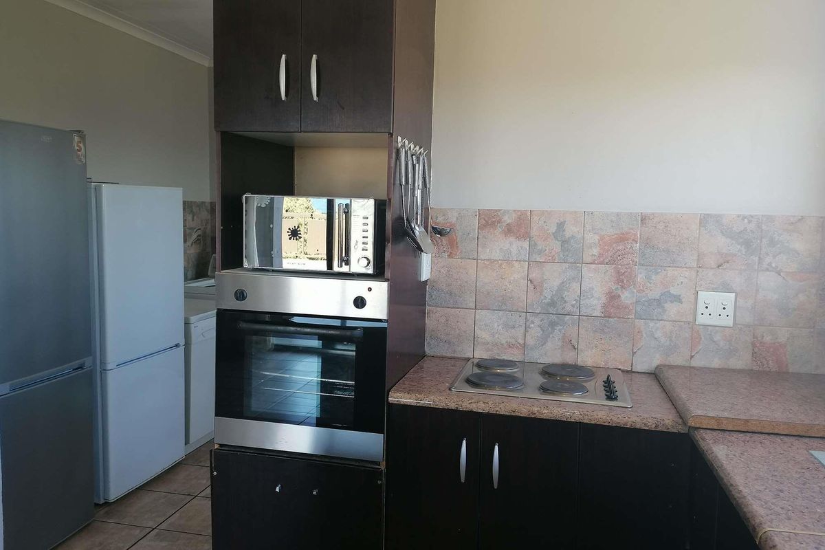 Functional kitchen featuring dark wood cabinetry, built-in oven, electric hob, and tiled backsplash, offering a practical layout for daily cooking needs.