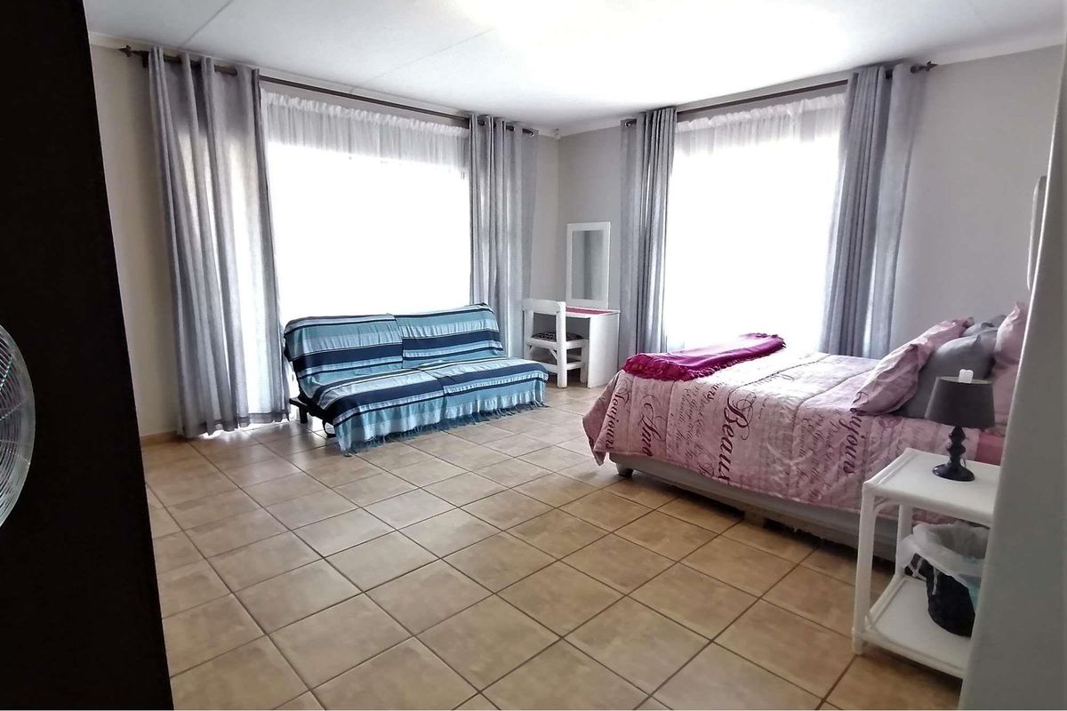Spacious bedroom featuring neutral wall tones, large windows with curtain rails, and durable tiled flooring throughout.