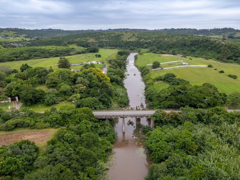 An aerial view of a rural landscape featuring a river, a bridge crossing, and surrounding green pastures and dense vegetation.
