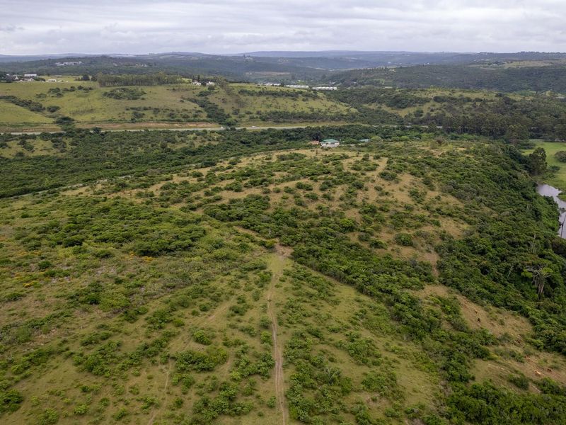 An aerial view of a large, undeveloped residential plot featuring natural vegetation, rolling hills, and scenic river frontage.