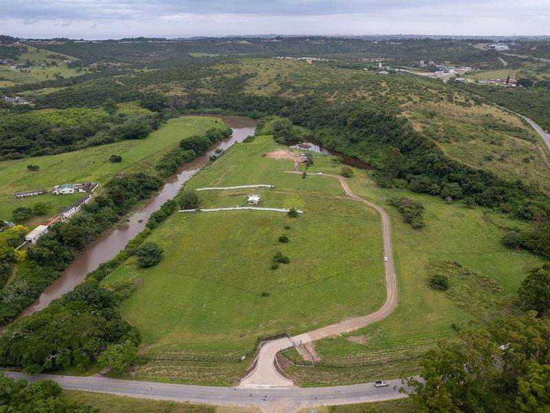 Aerial view of a large, expansive vacant residential plot featuring river frontage, established access roads, and perimeter fencing in a scenic landscape.